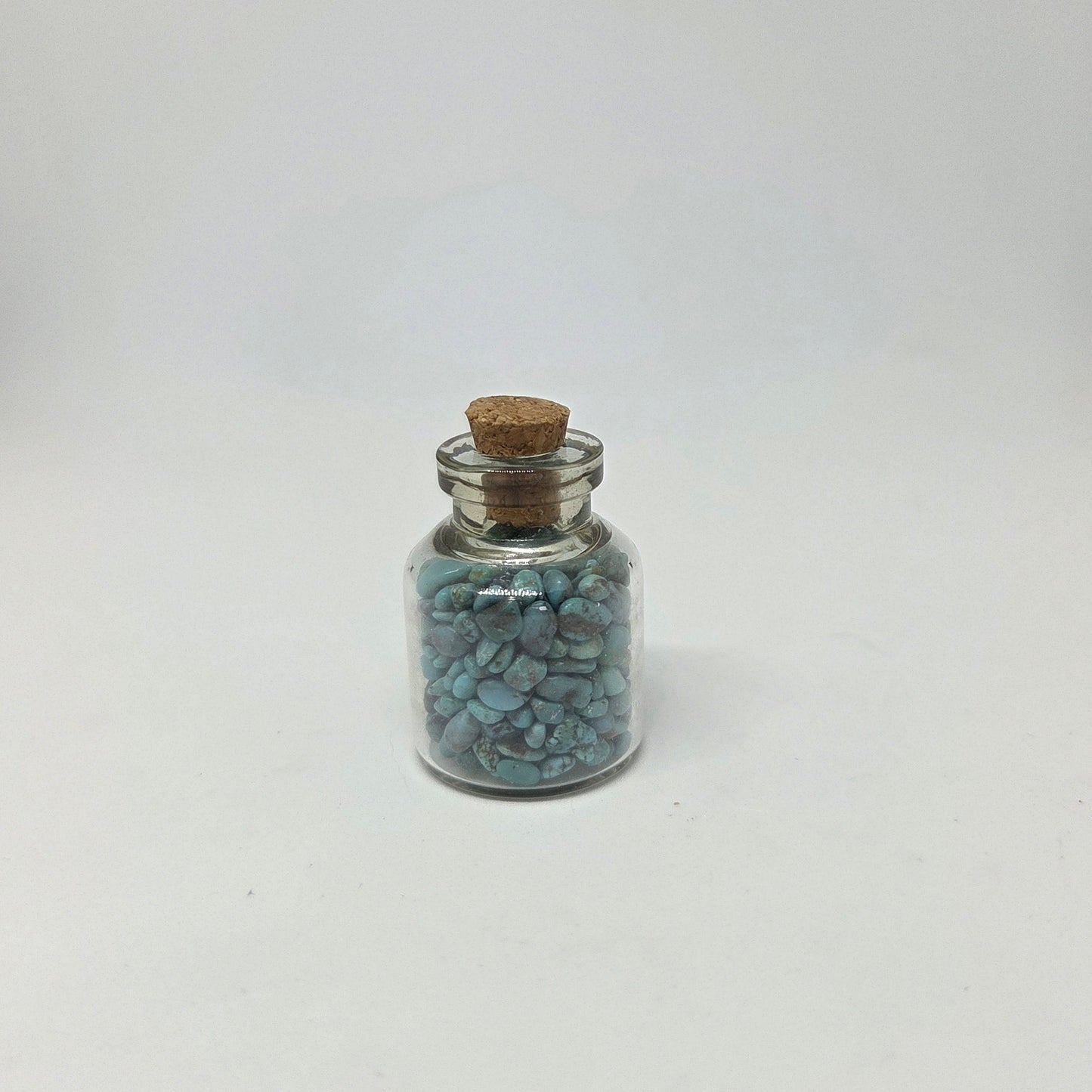 Small glass jar with cork lid containing blue stones on a white background