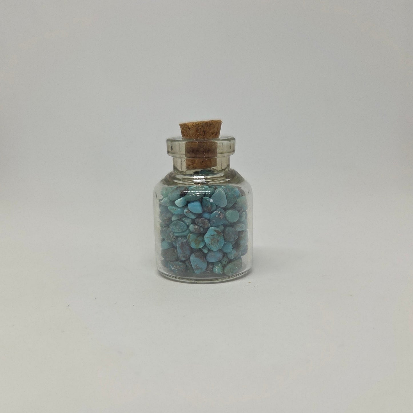 Small glass jar with cork lid containing blue stones on a light gray background