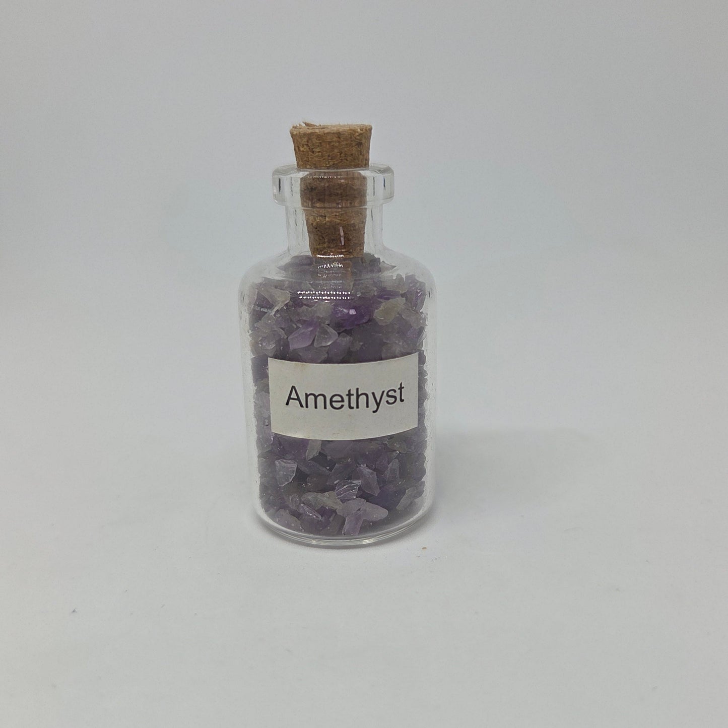 Small glass bottle filled with amethyst crystals on a white background