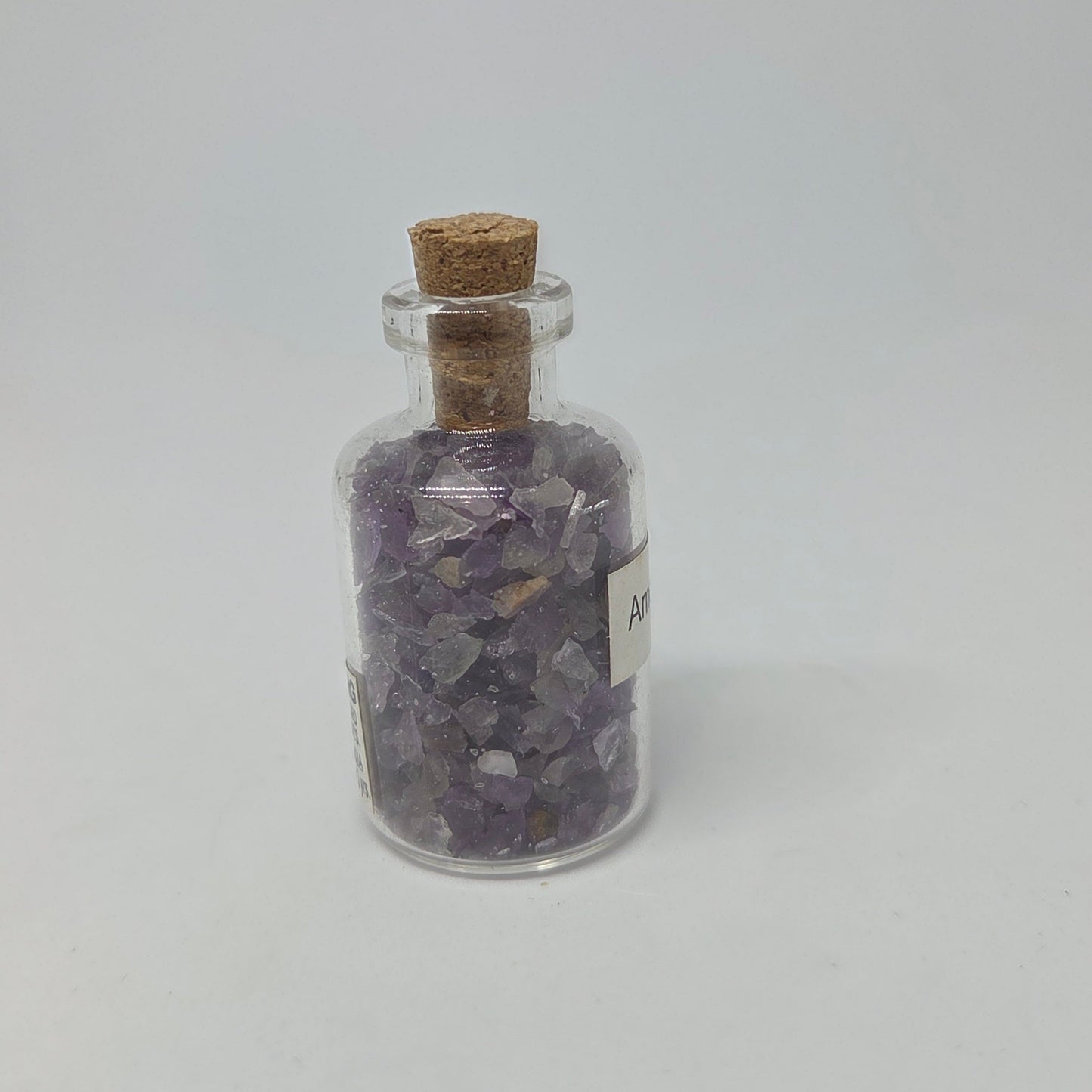 Glass jar with cork lid containing purple crystals on a white background
