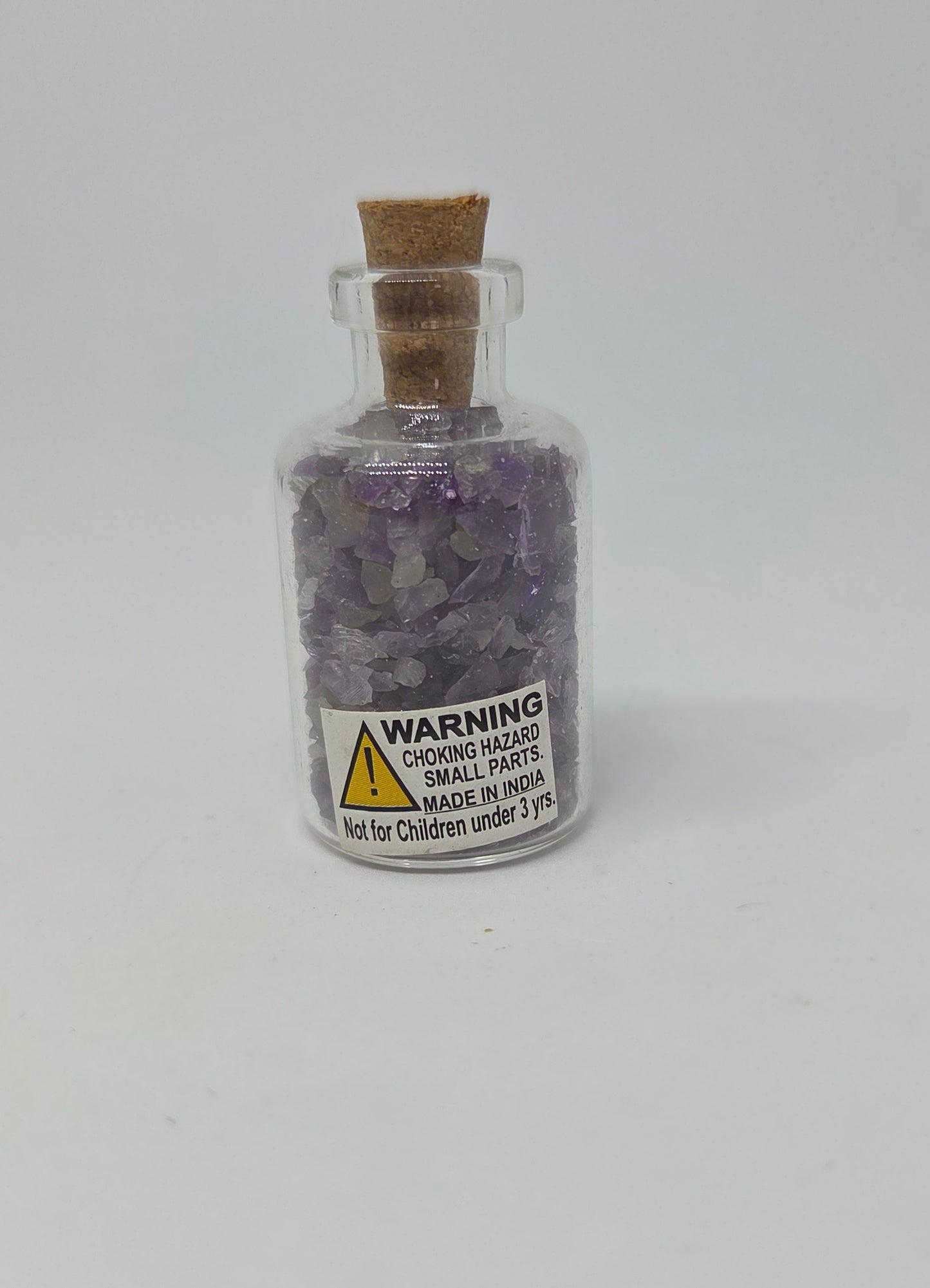 Small glass bottle with cork lid containing purple crystals on a white background