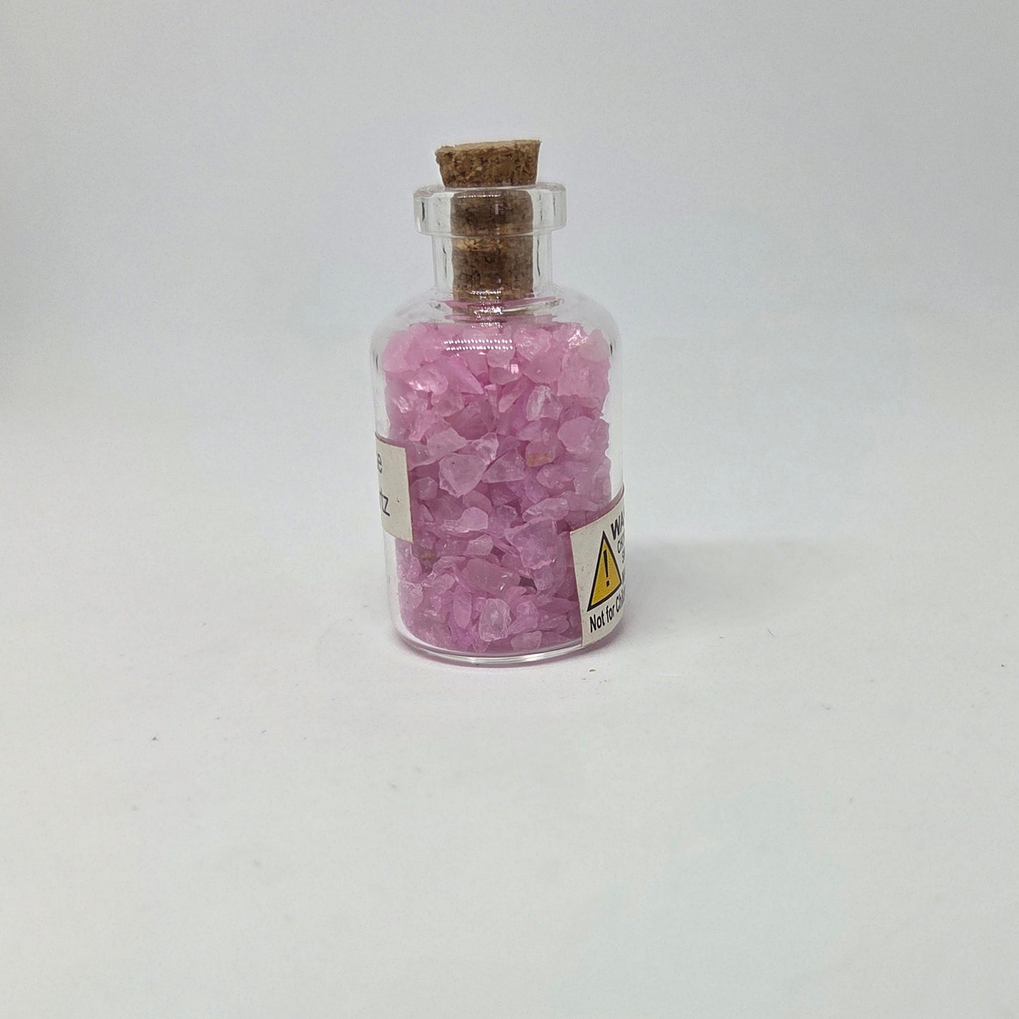 Small glass bottle filled with pink crystals on a white background