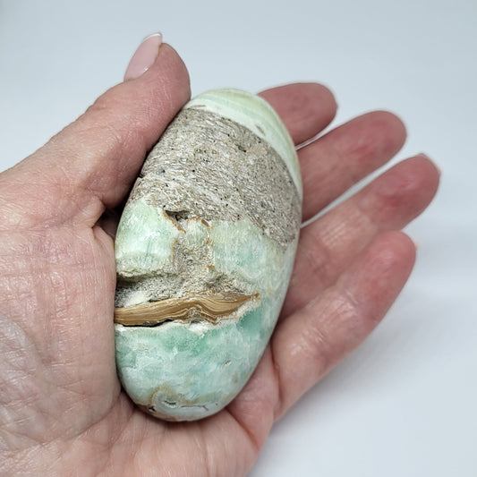 A person holding a Caribbean Calcite palm stone with ocean blue and white color bands.