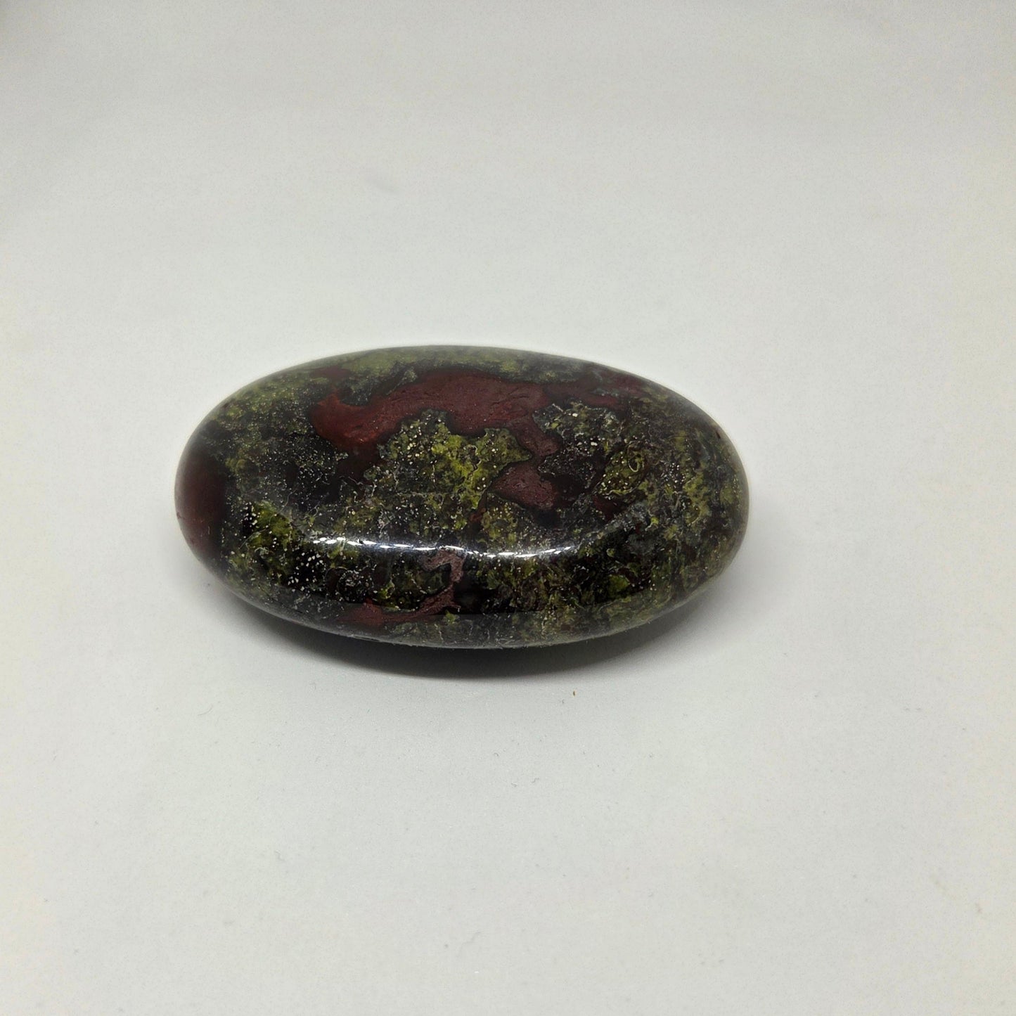 Oval-shaped stone with green and red patterns on a white background