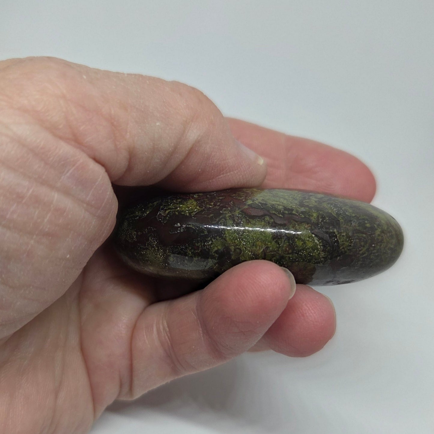 Hand holding a polished green stone against a white background