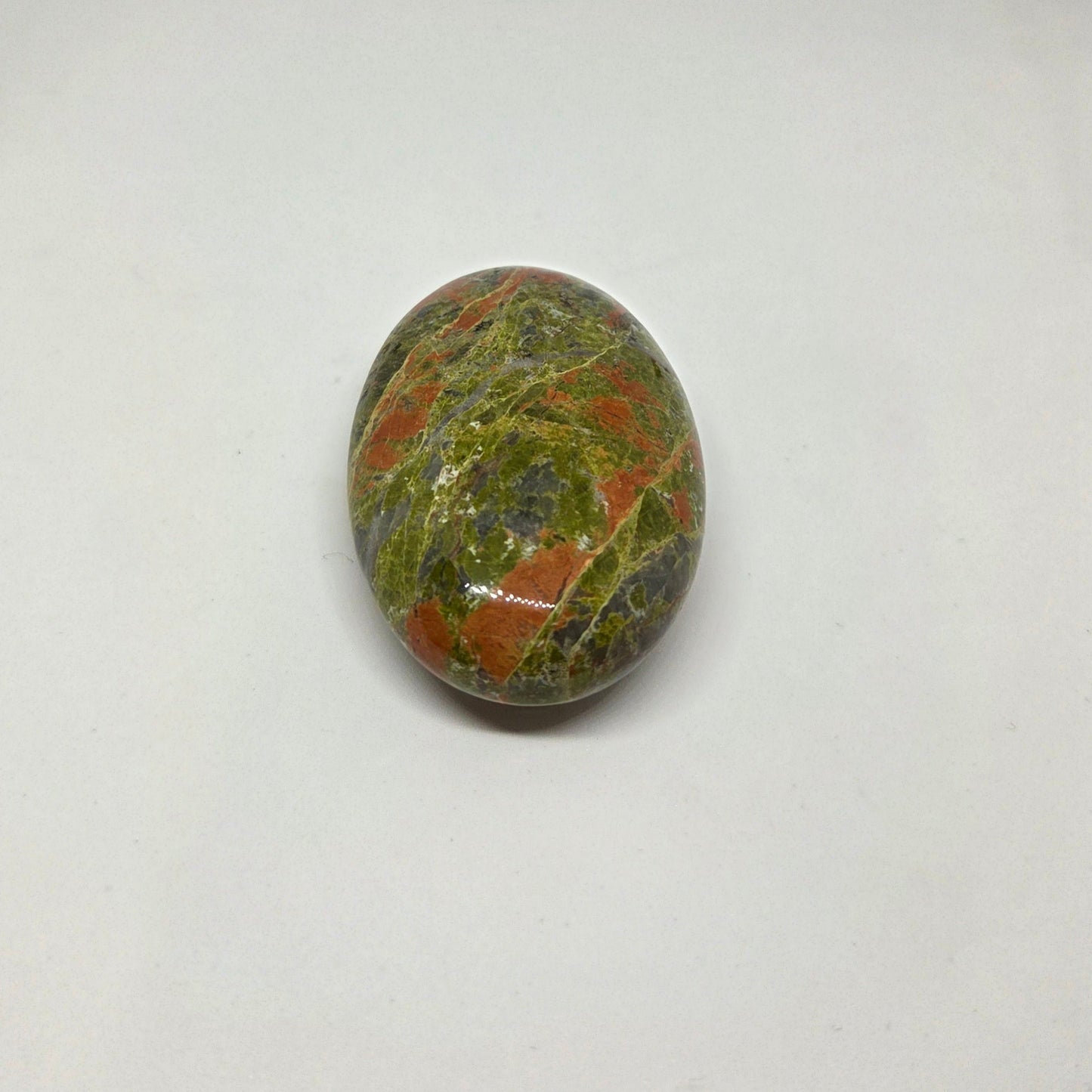 Oval-shaped gemstone with green, brown, and black patterns on a white background