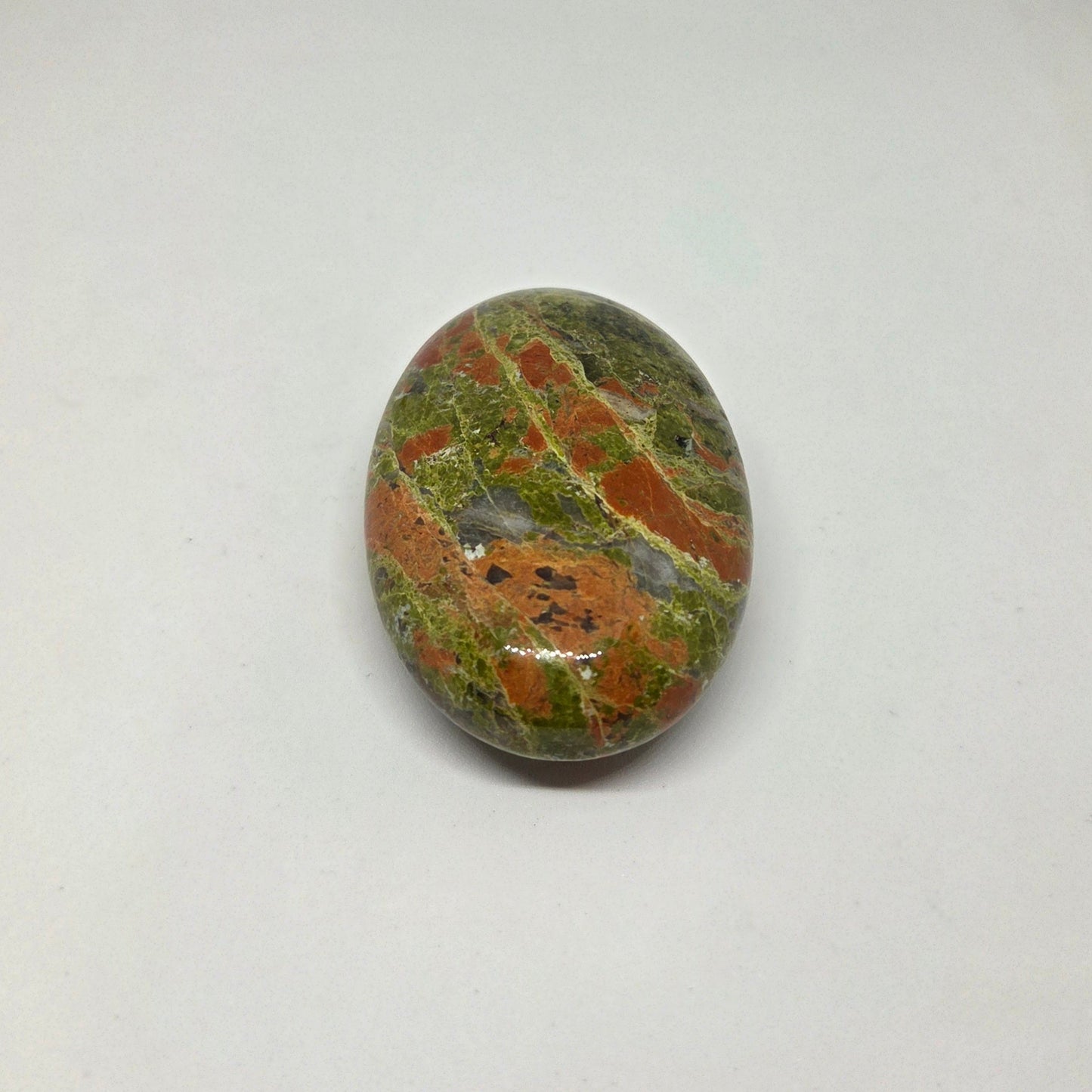 Oval-shaped stone with green and brown patterns on a white background