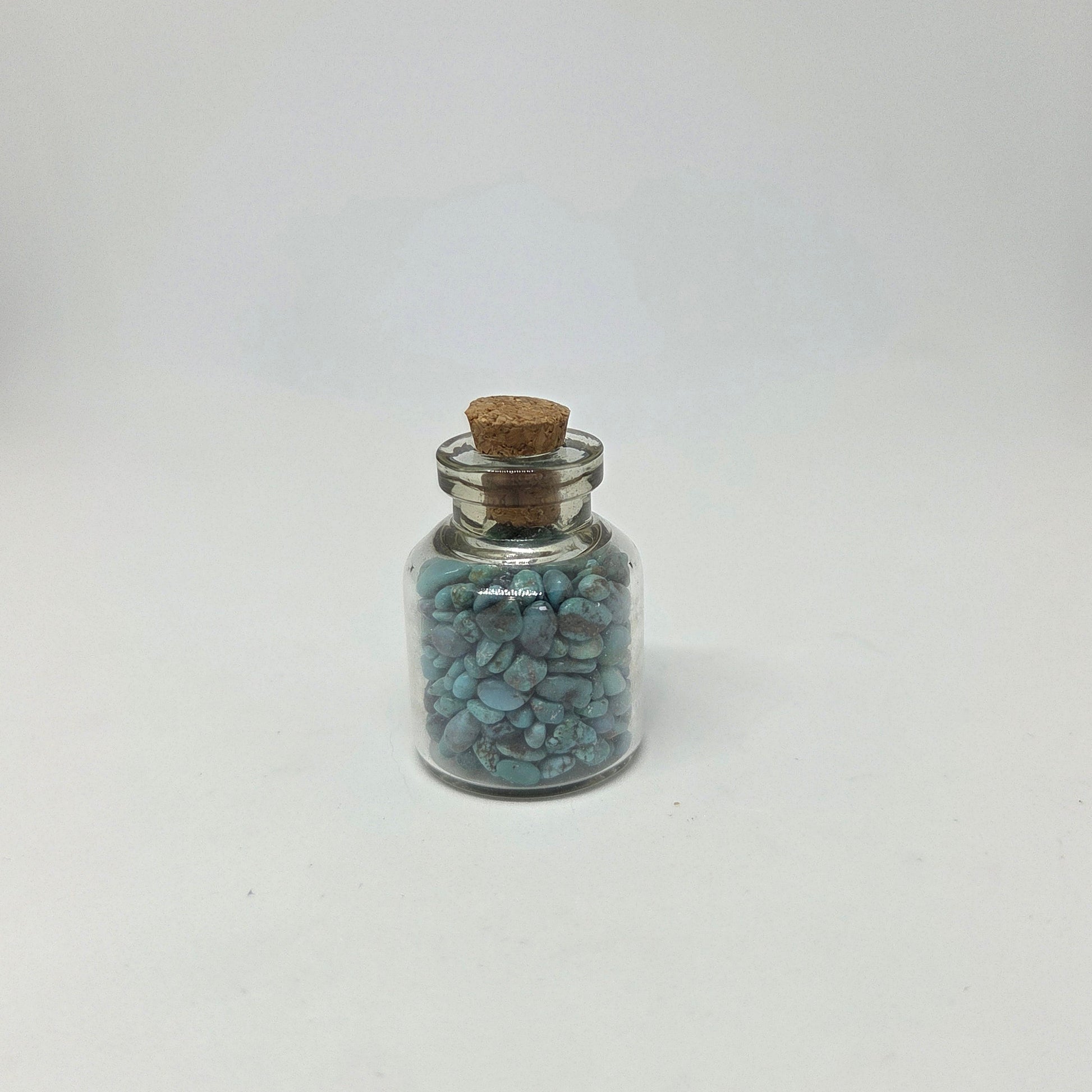 Small glass jar with cork lid containing blue stones on a white background