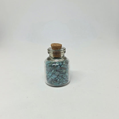Small glass jar with cork lid containing blue stones on a white background