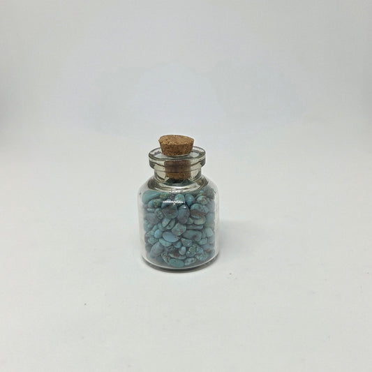 Small glass jar with cork lid containing blue stones on a white background