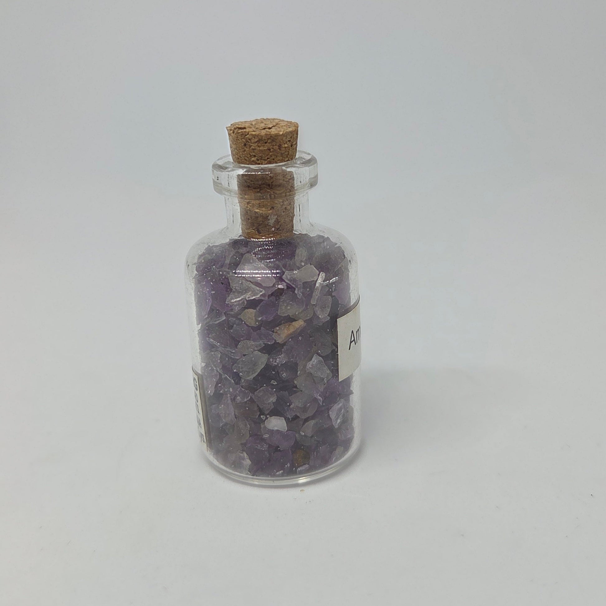 Glass jar with cork lid containing purple crystals on a white background