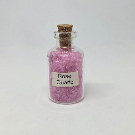 Small glass jar filled with pink rose quartz crystals on a white background