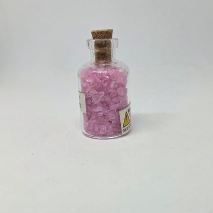 Small glass bottle filled with pink crystals on a white background