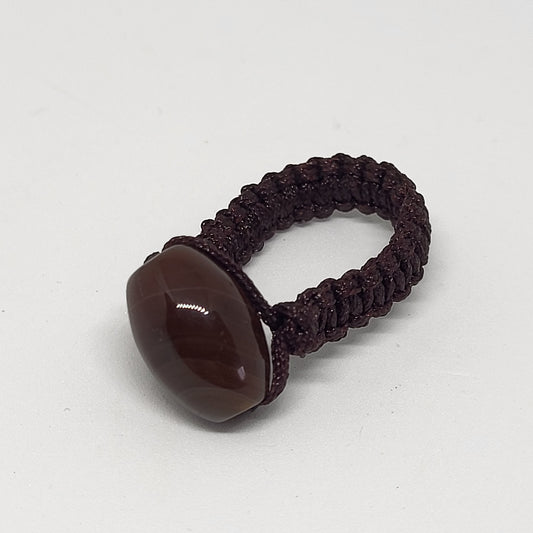 A brown carnelian macrame ring on a white background, the stone is oval-shaped and the band is woven macrame.
