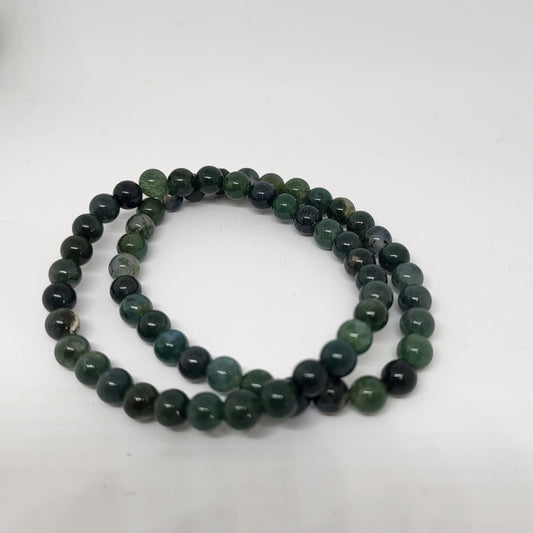 A moss agate bracelet with round beads in shades of green and black, laid out on a white surface.