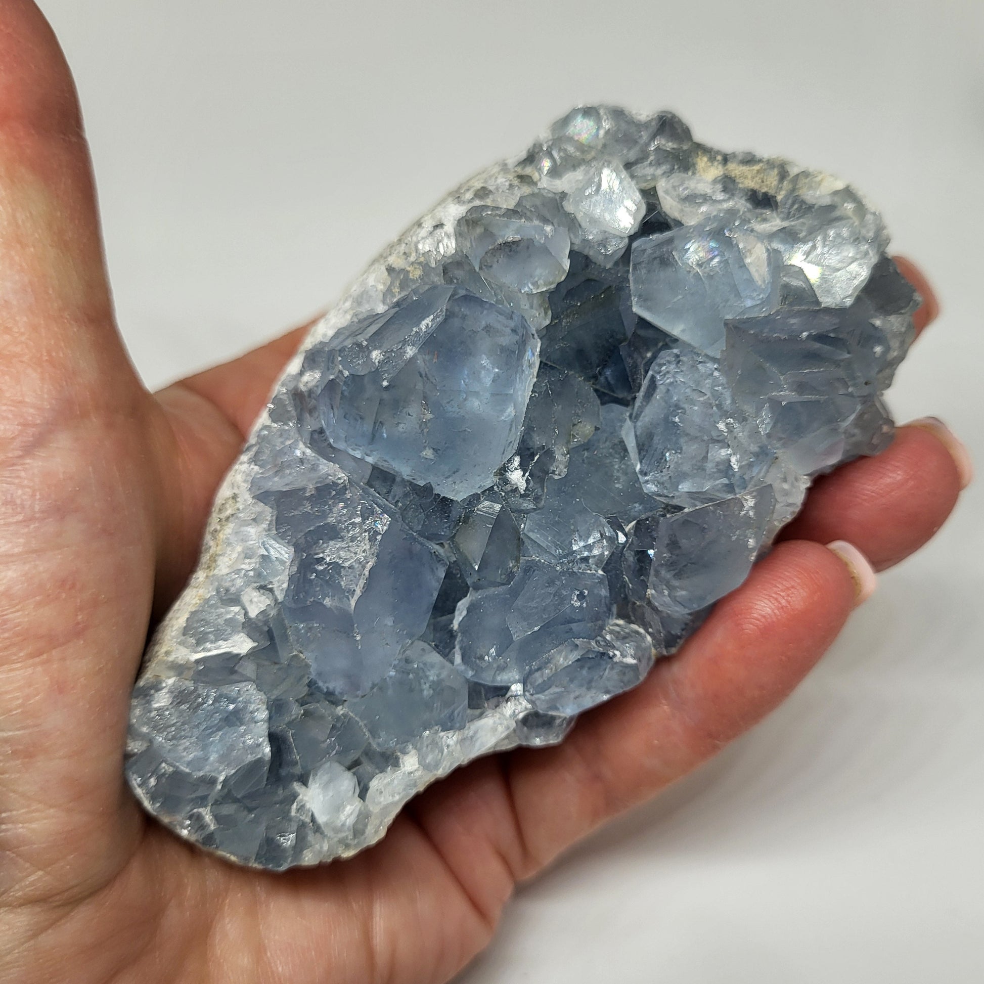 A person holding a raw celestite crystal with a pale blue color.