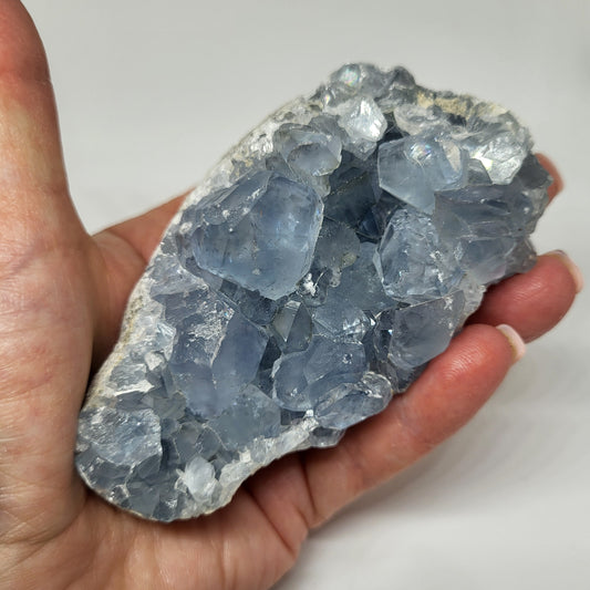 A person holding a raw celestite crystal with a pale blue color.